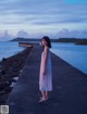 A woman in a white dress standing on a pier by the water.