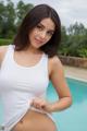 A woman in a white tank top posing by a pool.