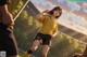 A woman in a yellow shirt and black shorts playing soccer.