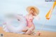 A woman in a pink bathing suit and hat sitting on a beach.